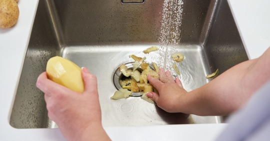 man putting potato peels down the garbage disposal
