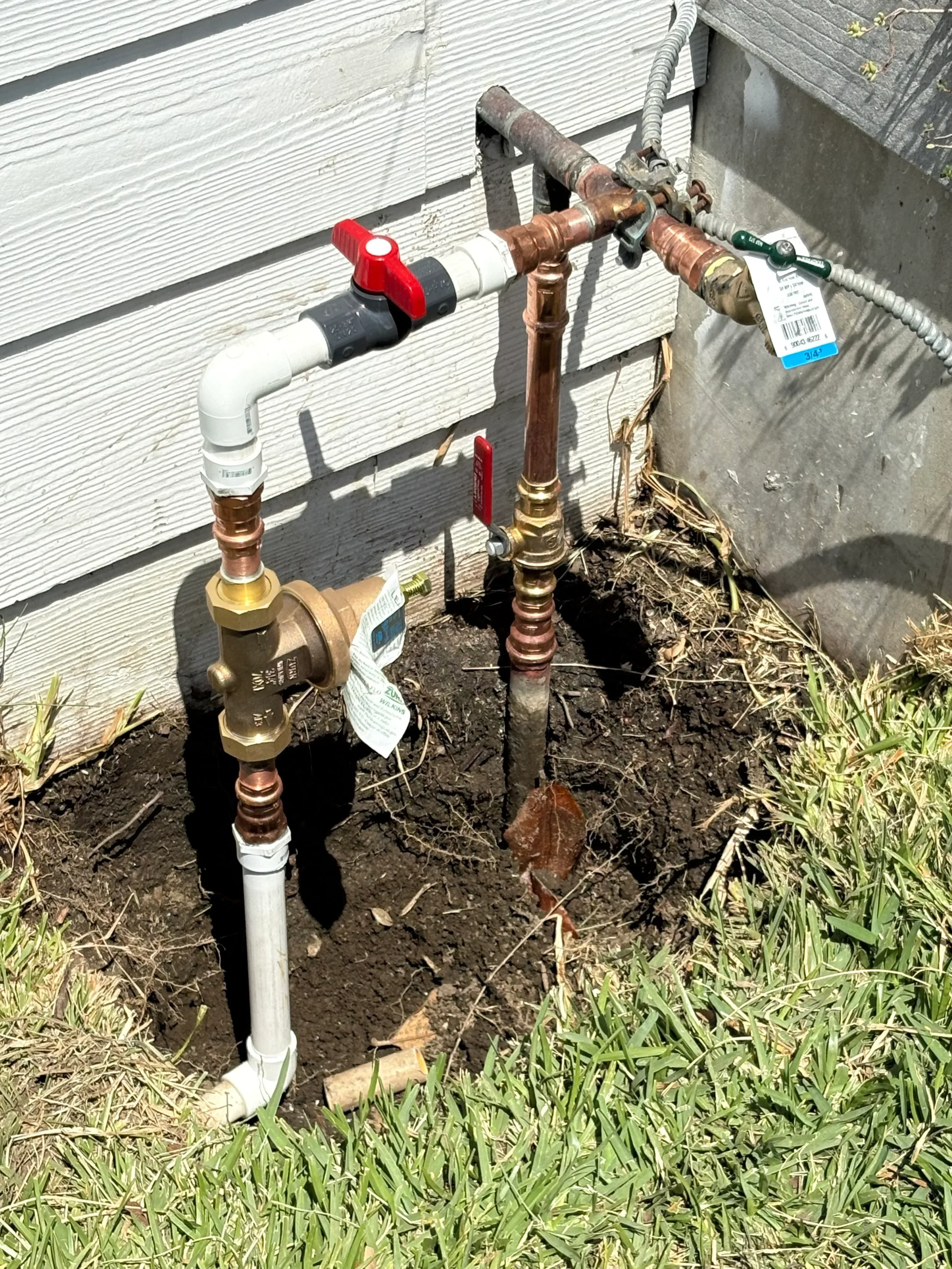 Copper water lines with brass fittings and red ball valve installed on concrete pad