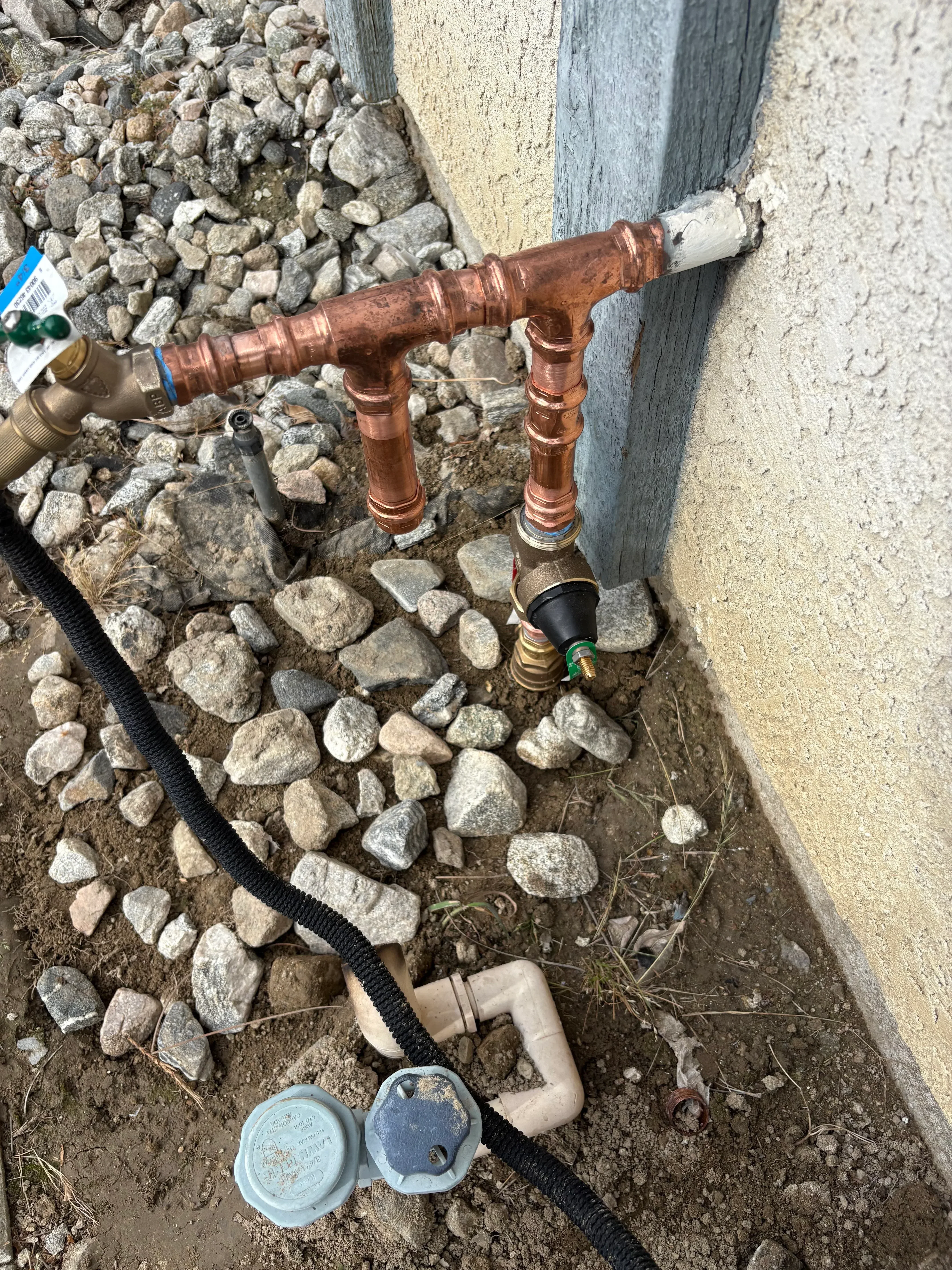 Copper manifold with dual valves, brass fittings, and black poly tubing on gravel base