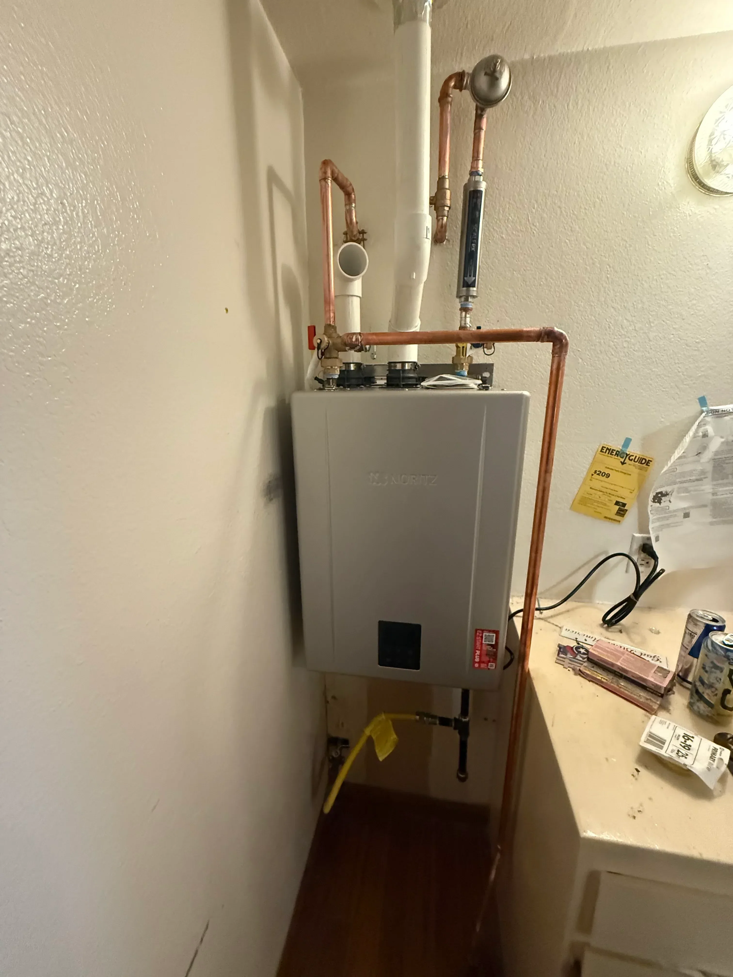 Tankless water heater with copper piping, pressure gauge, and digital control panel installed in utility space