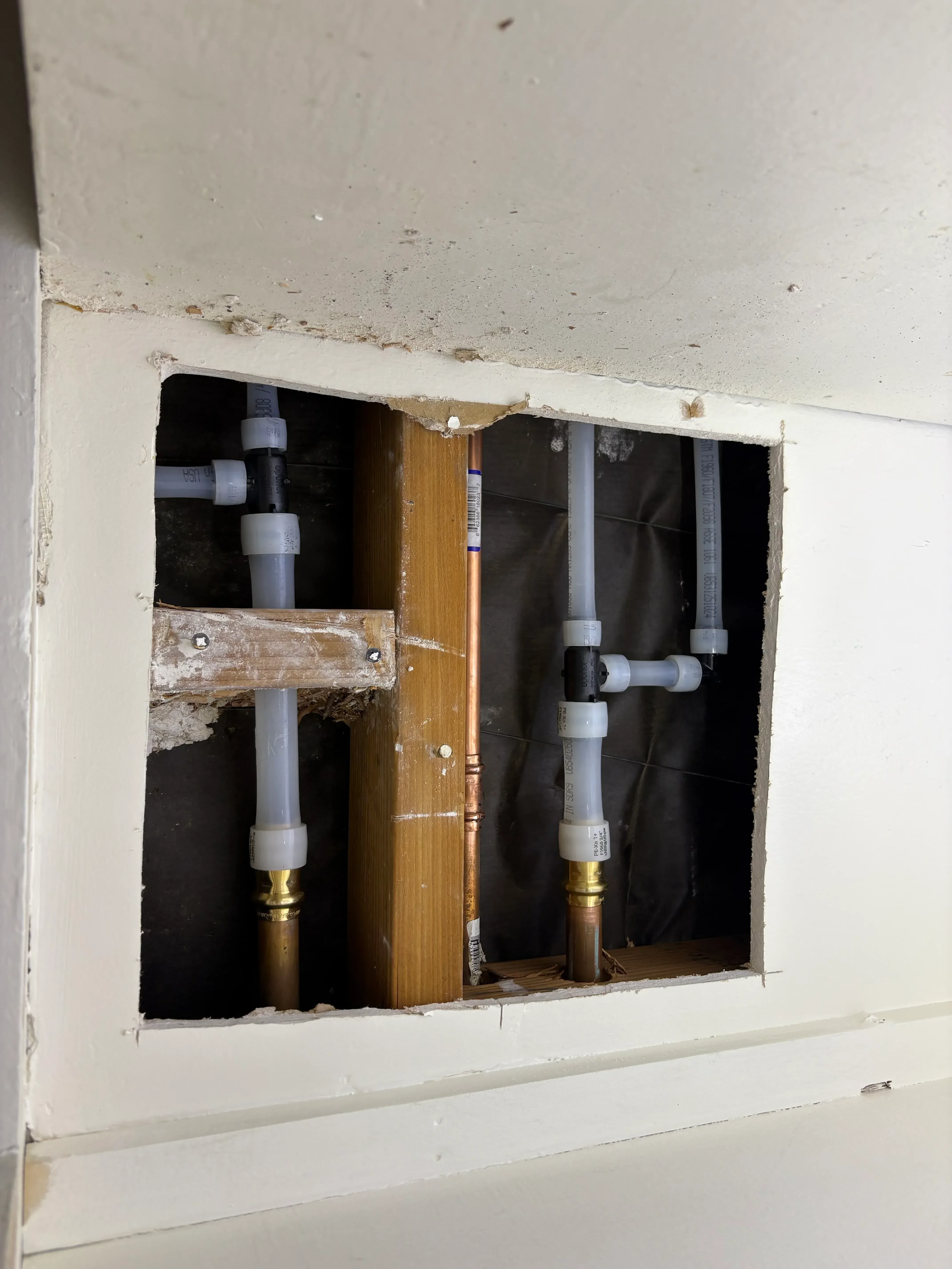 PEX water lines with brass fittings and white couplings installed in wall framing